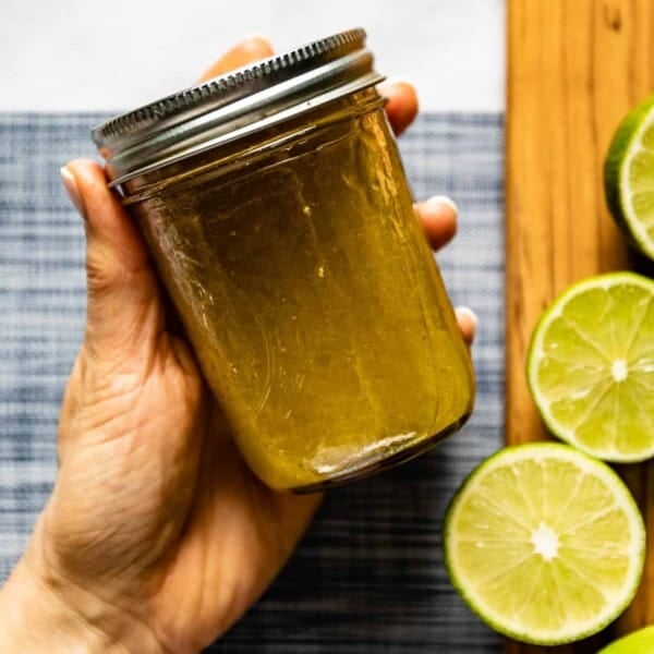 Person holding a jar or honey lime dressing in her hand.