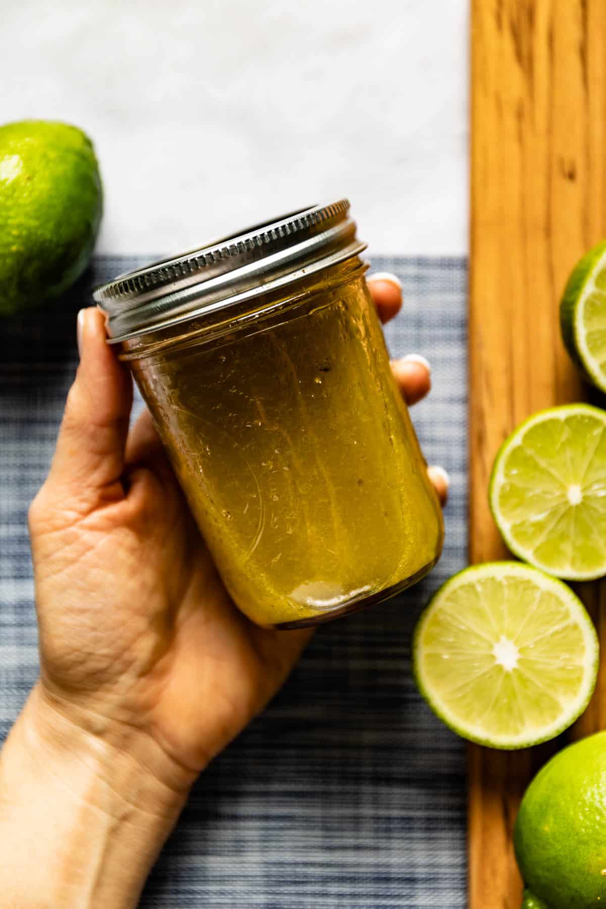 Person holding a jar of honey lime vinaigrette in her hand with fresh lime around it.