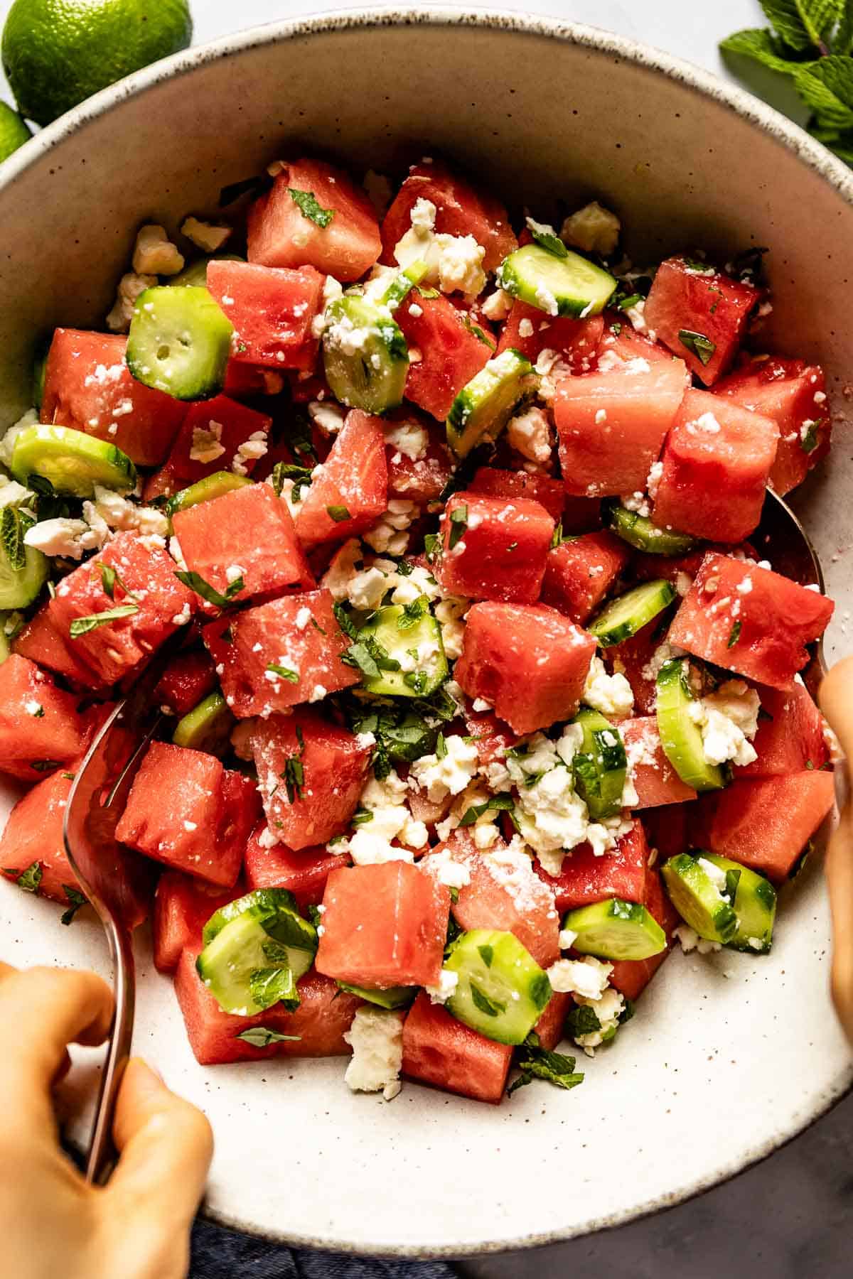 Watermelon cucumber salad in a bowl being stirred by a woman from the top view.