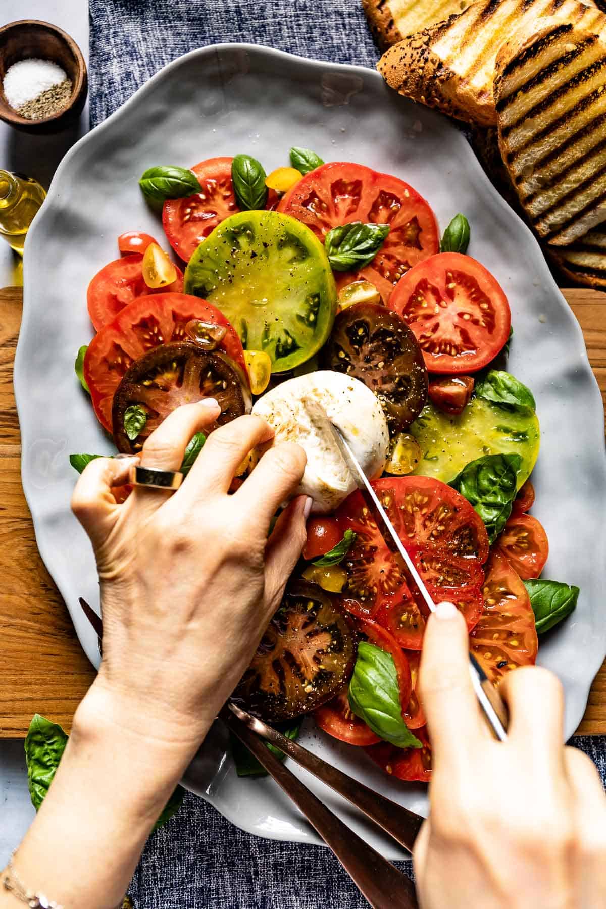 Person cutting the burrata in burrata caprese salad from the top view.