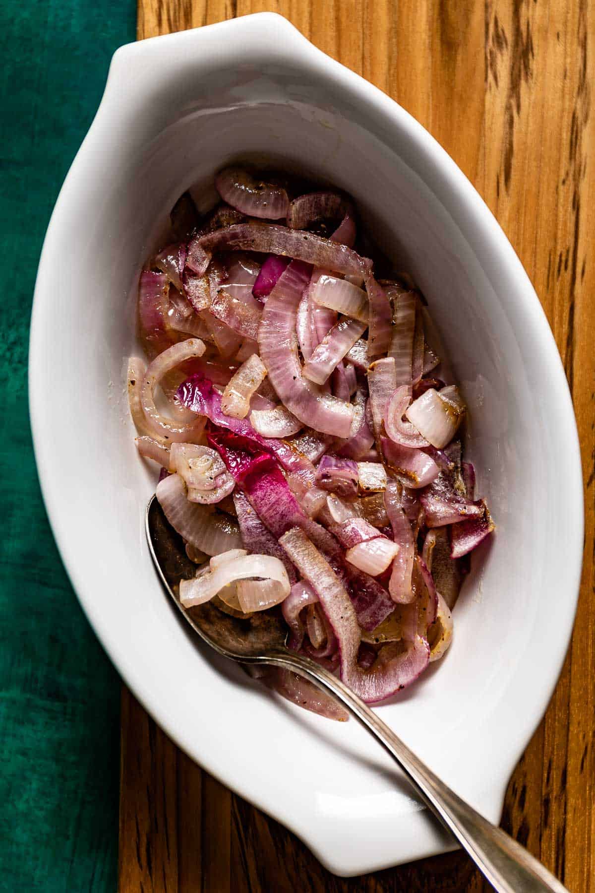 Roasted red onion slices in a bowl with a spoon on the side.