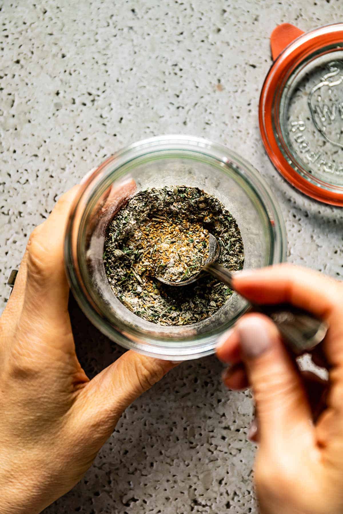 Person mixing Mediterranean spices in a jar from the top view.