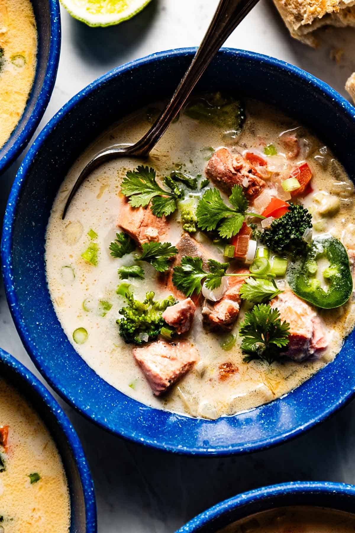 Salmon coconut soup garnished with cilantro in a bowl with a spoon on the side.