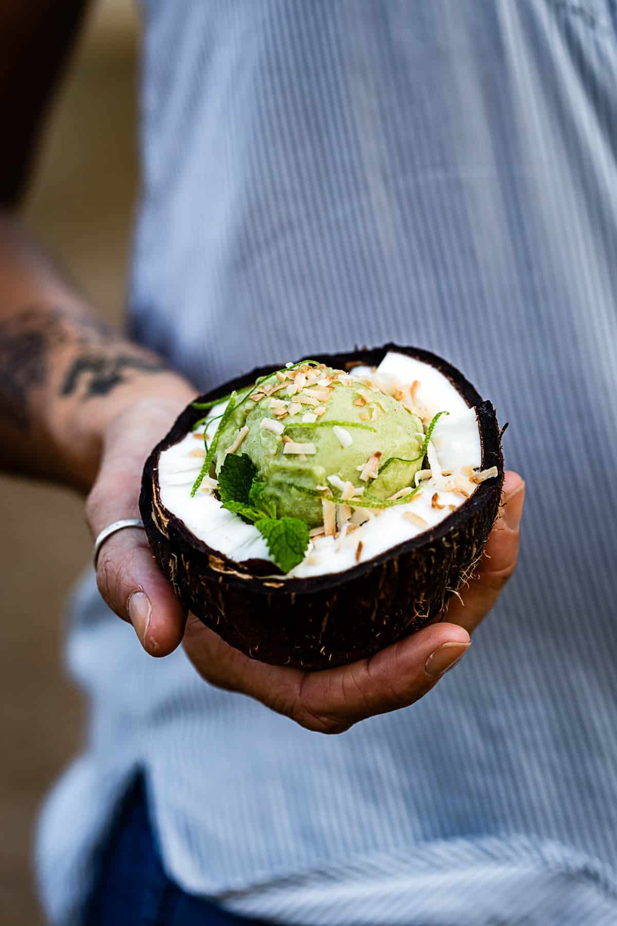 Person holding guacamole ice cream in a coconut bowl from the front view.