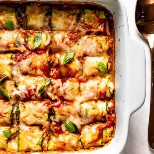 Zucchini lasagna rolls in a baking dish lay on white table from the top view.