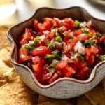 A bowl of salsa from cherry tomatoes with chips on the side.