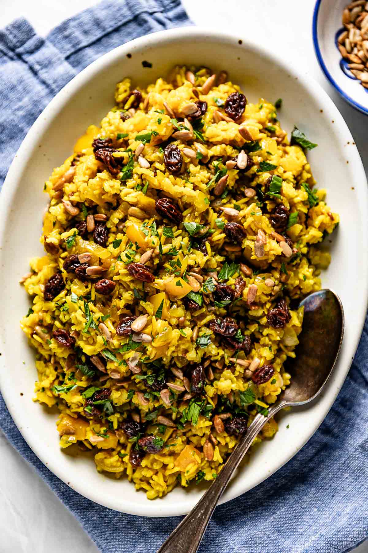 Curried brown rice on a plate garnished with raisins and sunflower seeds.