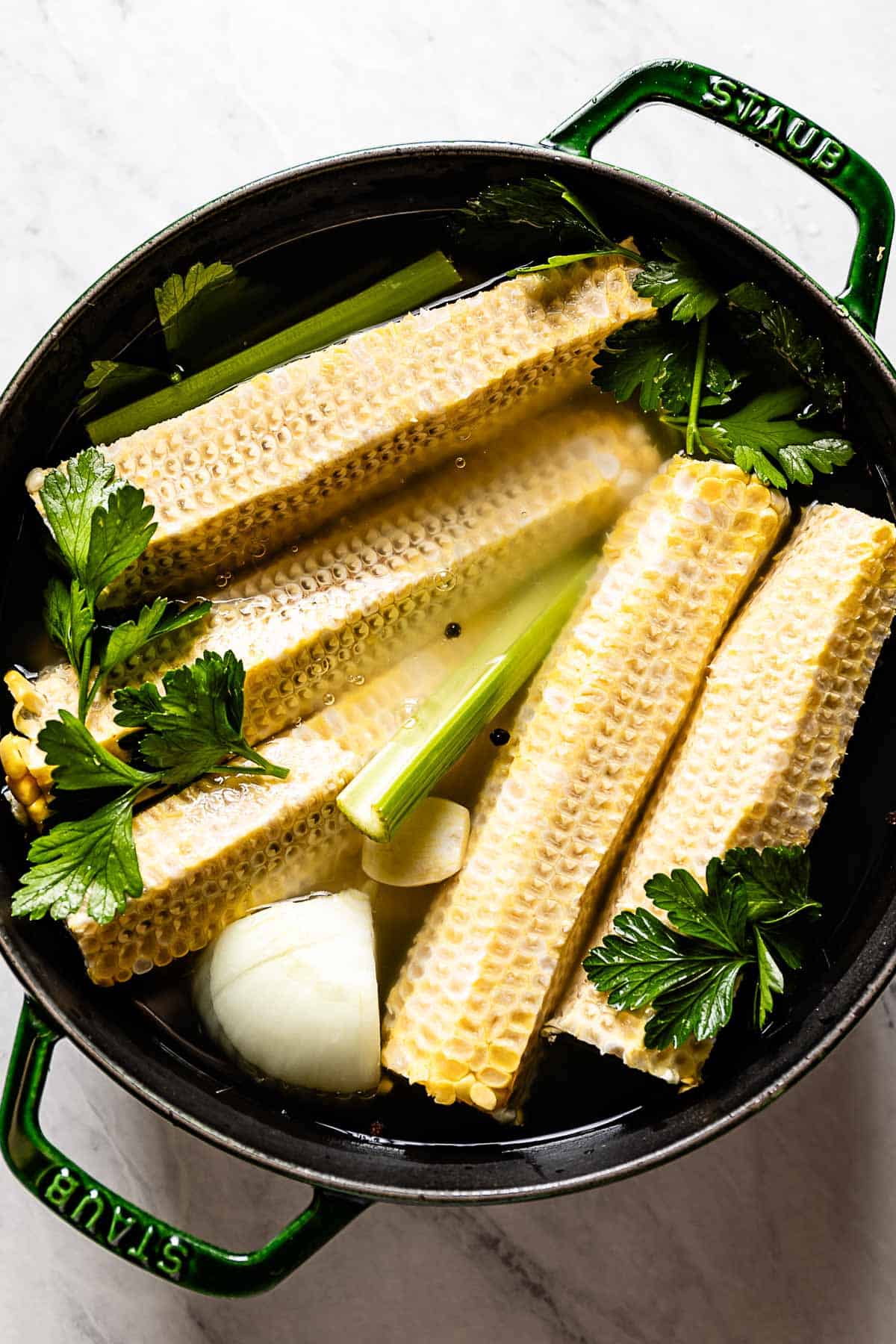 Corn cobs, celery, parsley, and whole black peppercorns in a pot.