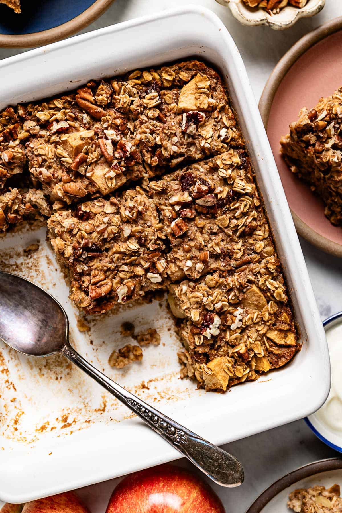 Baked apple oatmeal sliced in a square baking dish with a spoon on the side.