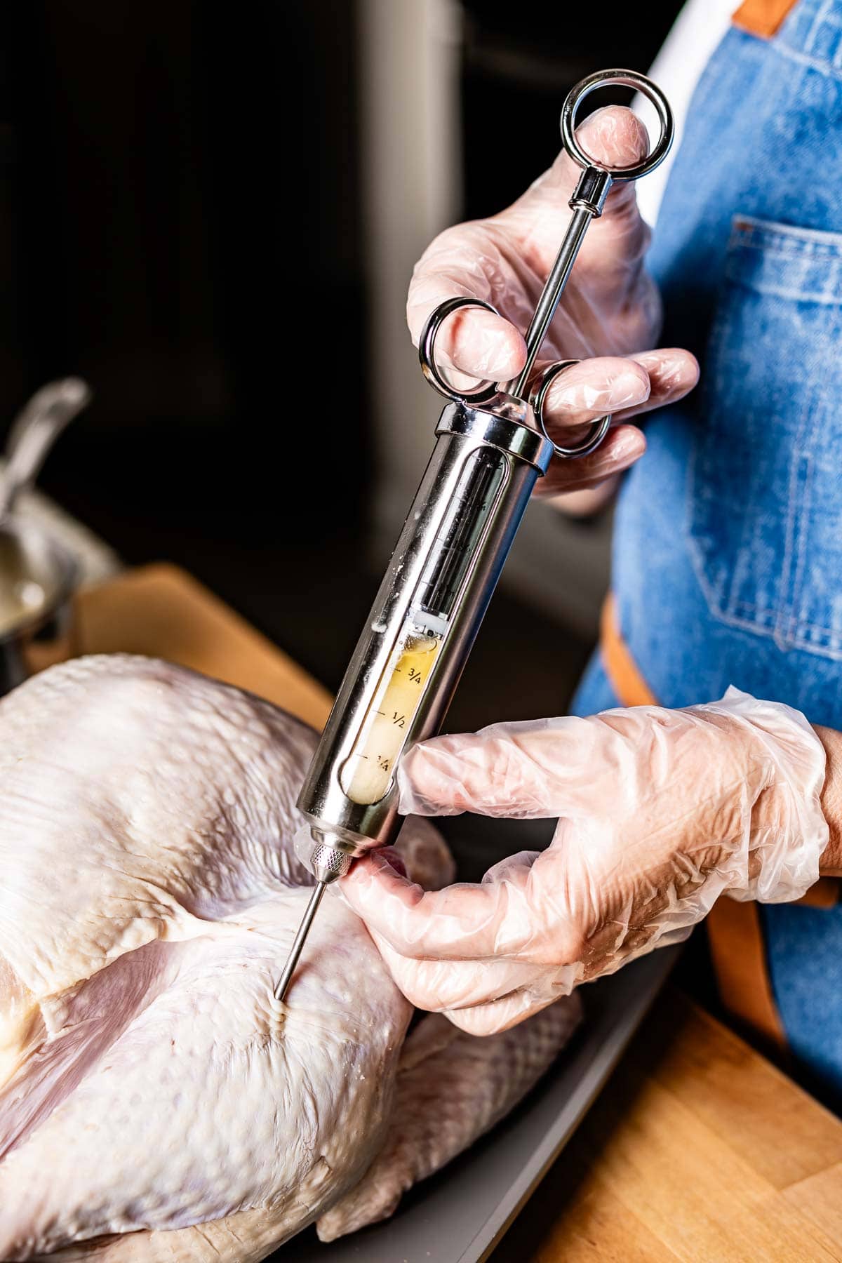 Person injecting garlic butter marinade into a turkey's thigh.