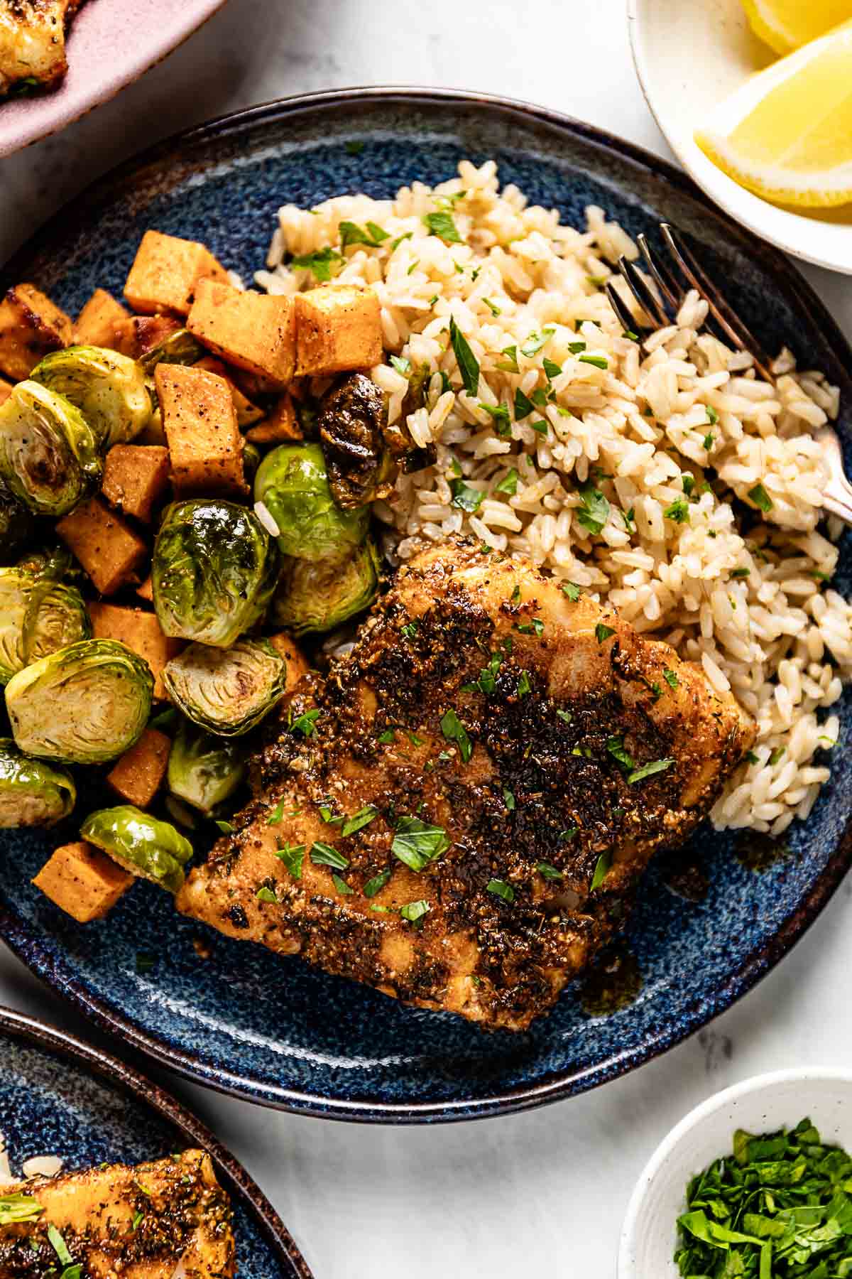 Baked blackened cod served with rice and roasted vegetables on a plate.
