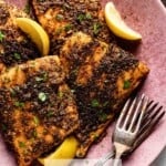 Seasoned cod on a plate with lemon wedges on the side.