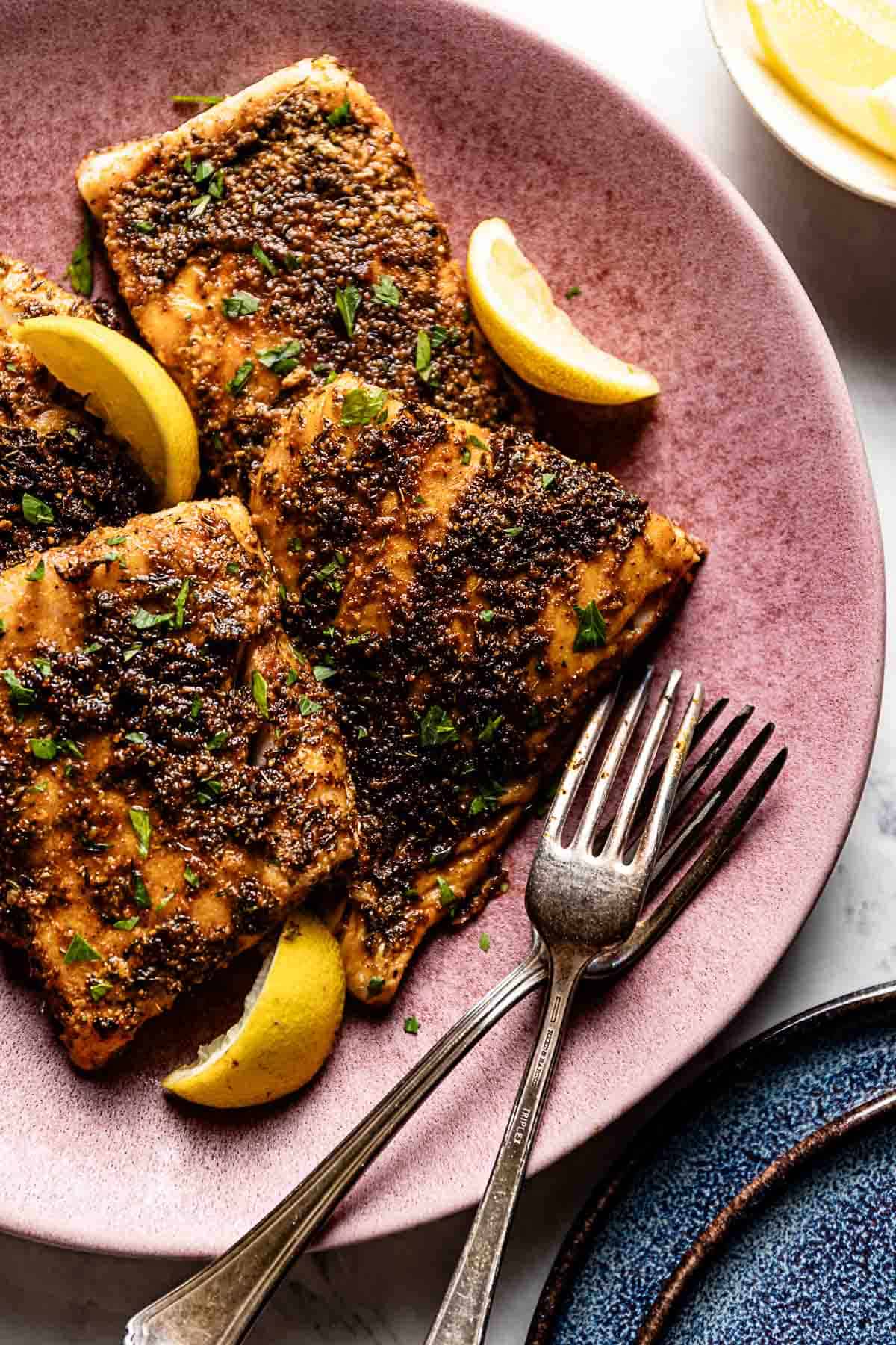 Blackened cod placed on a dish with lemon wedges on the side.