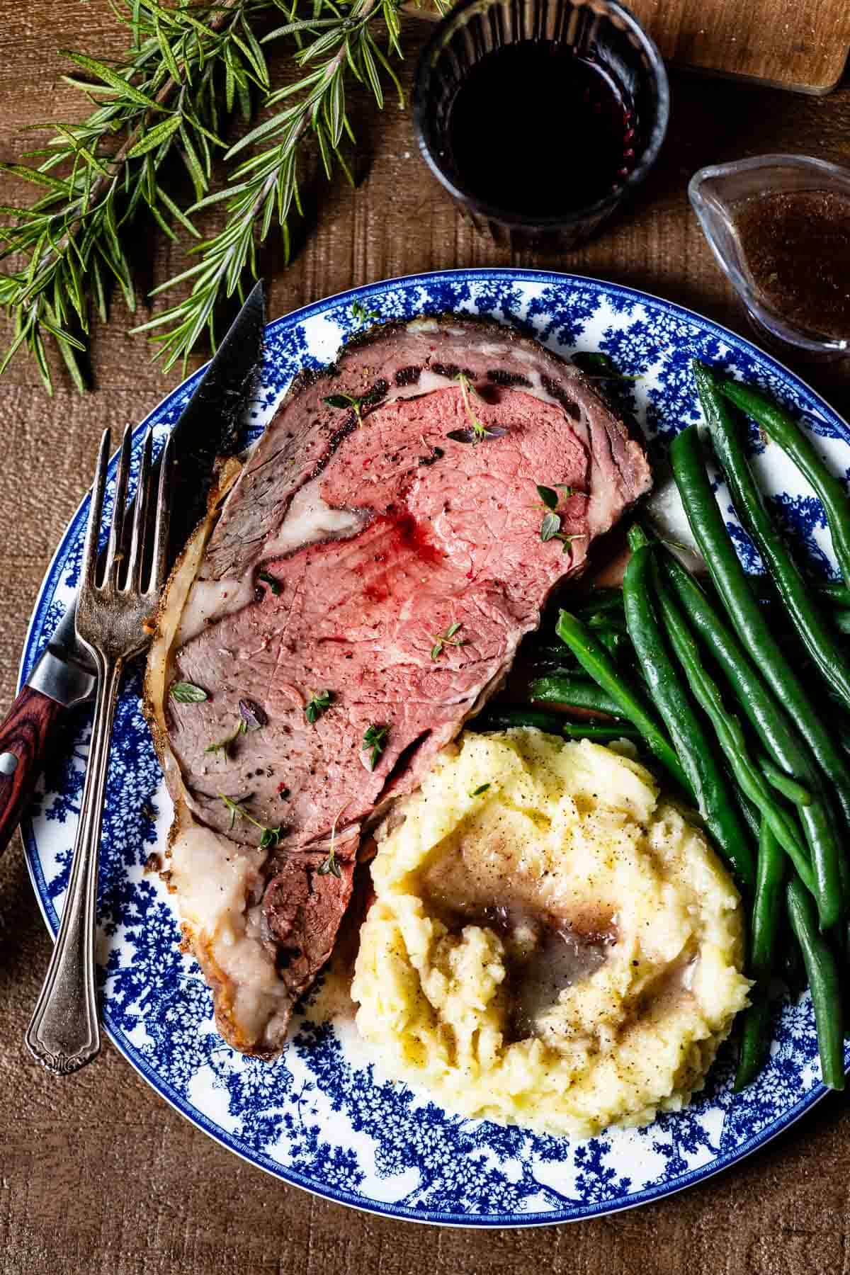 A slice of reverse seared standing rib roast served with mashed potatoes and green beans.