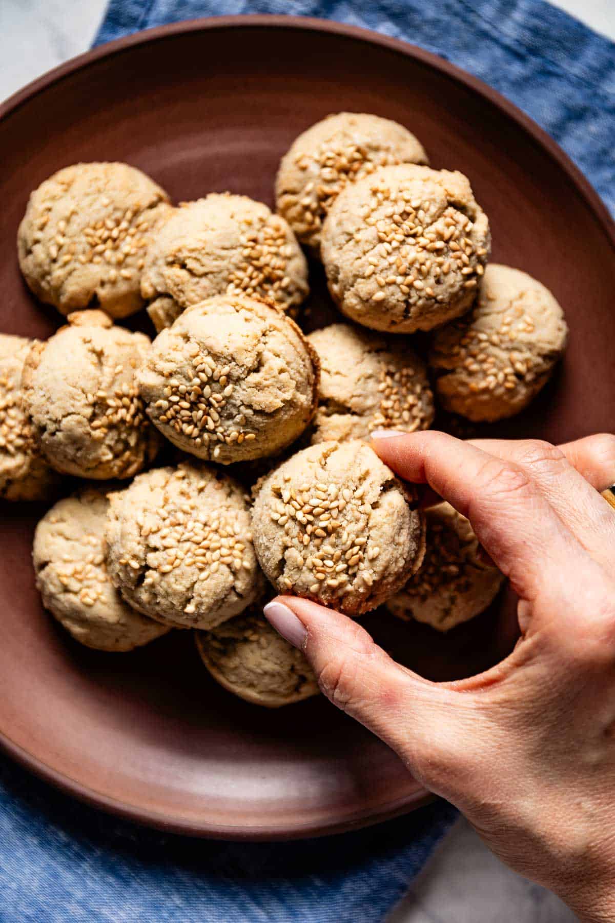 Almond flour tahini cookies on a plate from the top view with a person taking one from the plate.