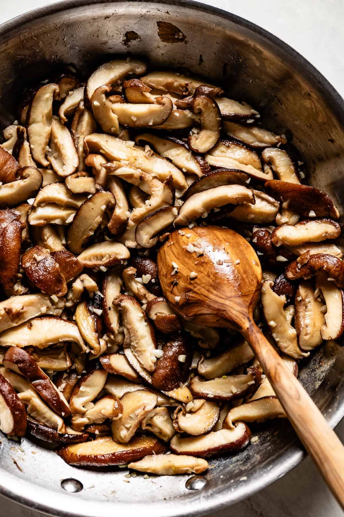 Shiitake mushrooms cooked in a skillet with a spoon on the side from the top view.
