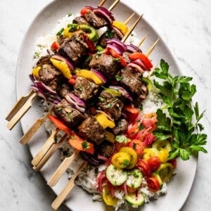 Baked beef kabobs on a bed of rice garnished with parsley from the top view.