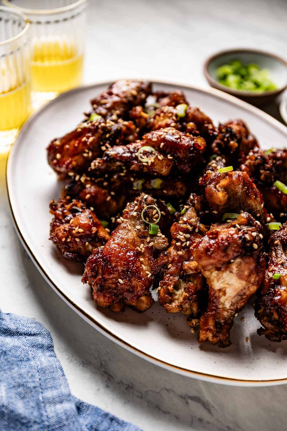 Sticky chicken wings garnished with sesame and green onions on a plate.