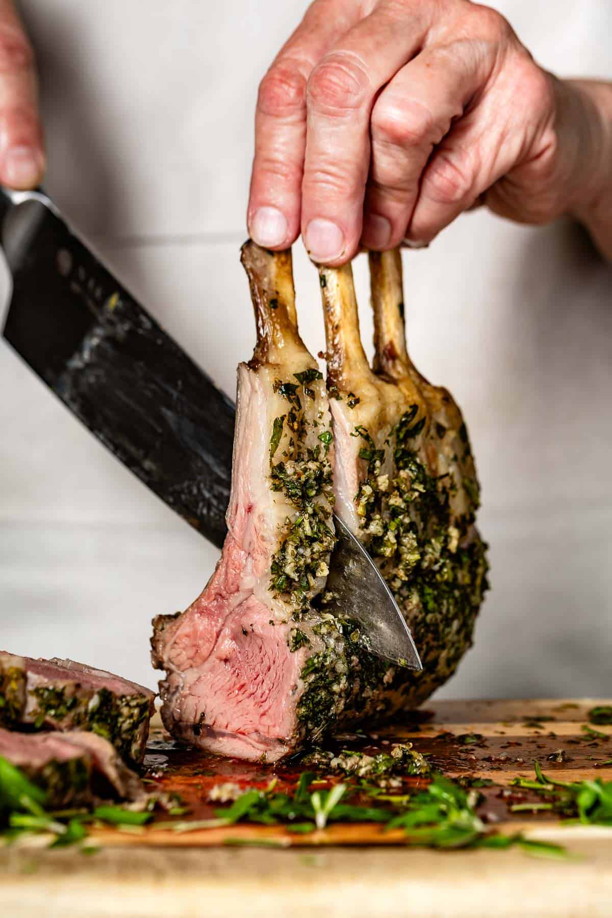 Person cutting a garlic and herb crusted lamb rib rack with a knife.