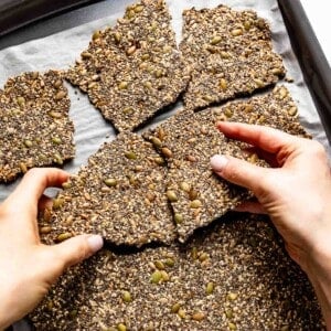 Person cracking freshly made seeded crackers from the top view.