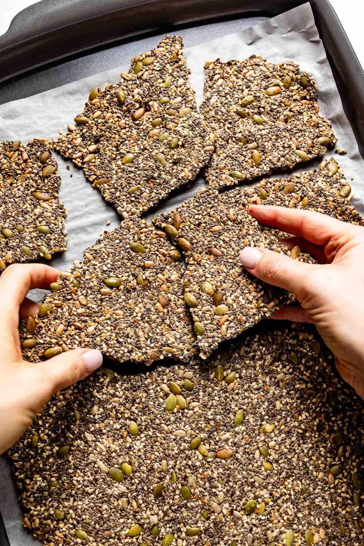 Person cracking seed crackers on a sheet pan.