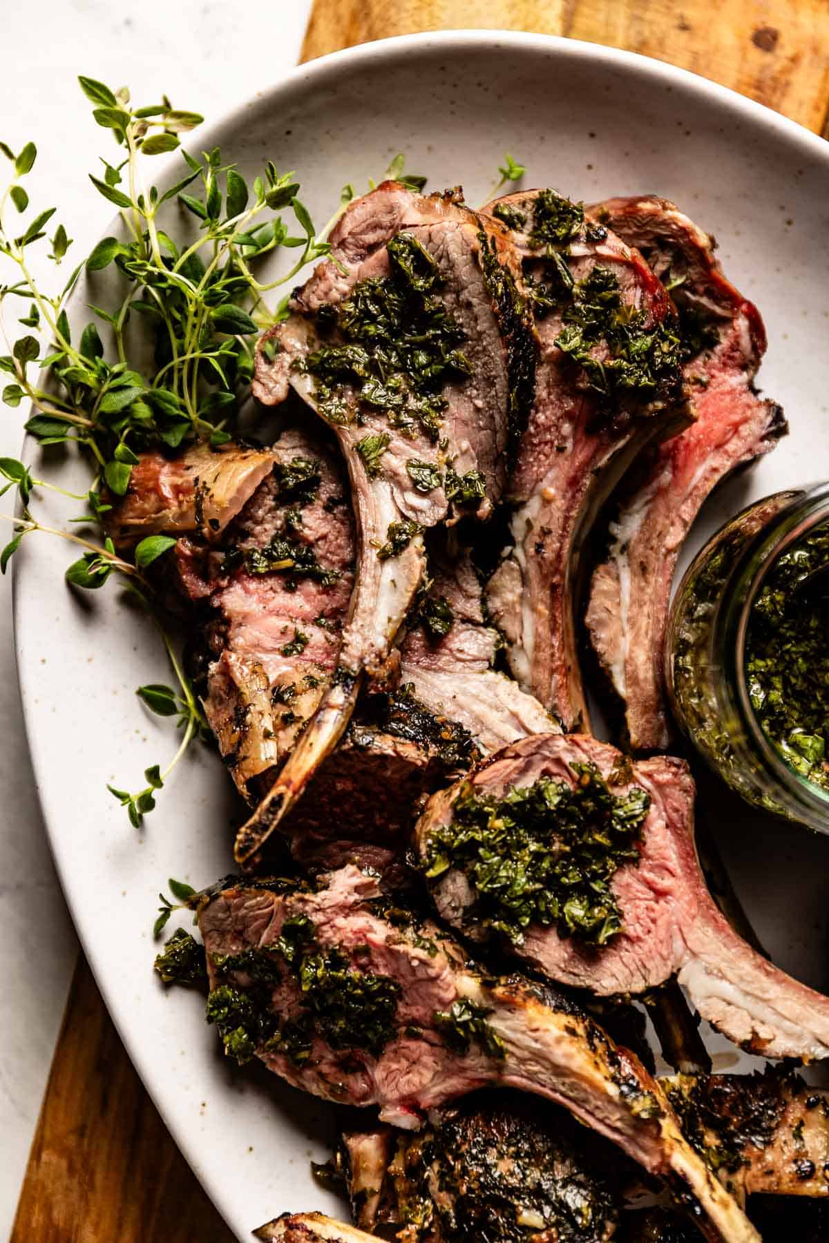 Barbecue rack of lamb on a plate garnished with thyme and mint sauce.