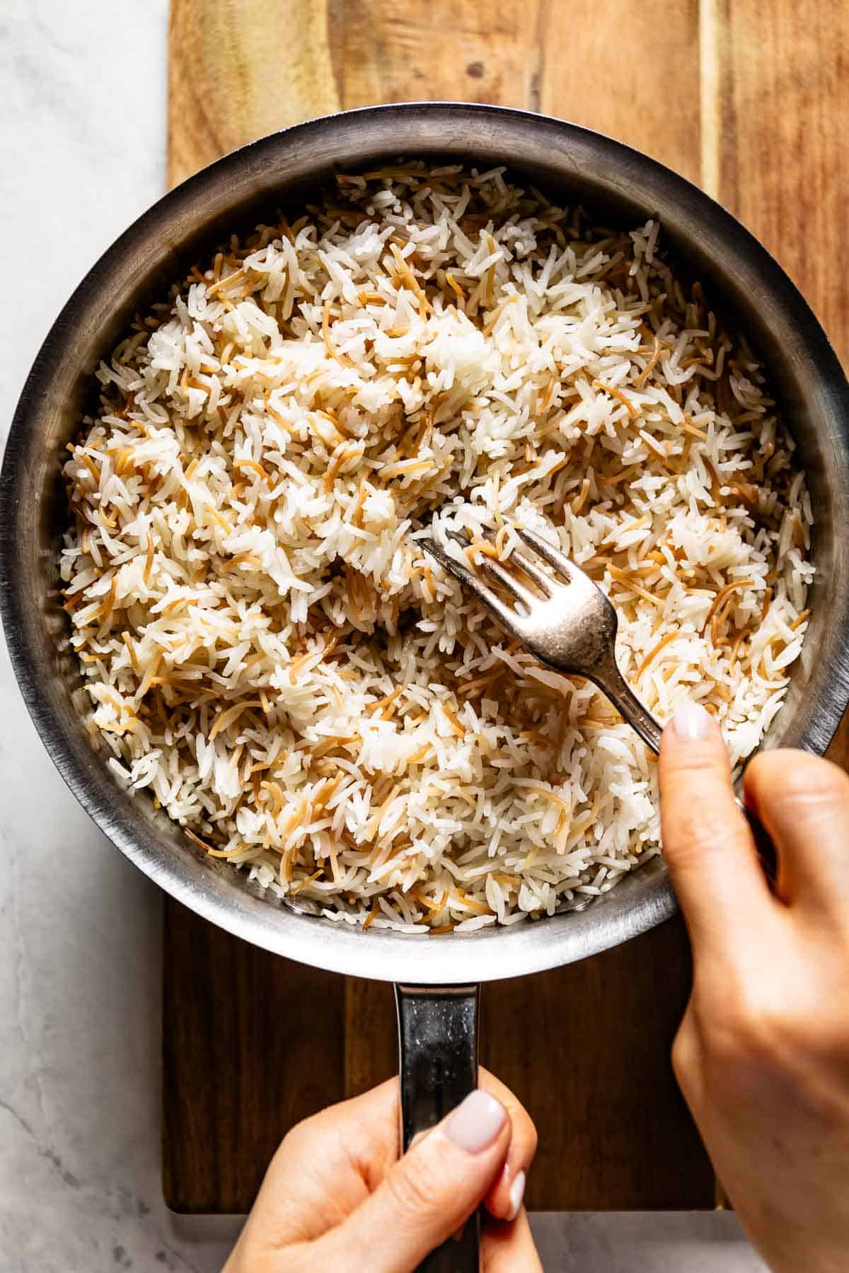 Person fluffing freshly cooked Lebanese rice with vermicelli.