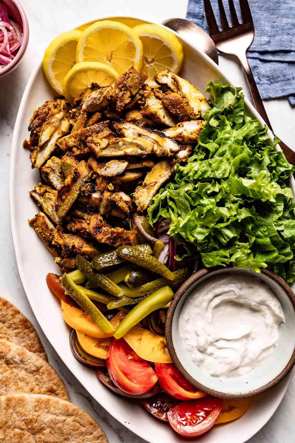 Mediterranean chicken shawarma served with pickles, lettuce, onion and tomatoes on a plate.