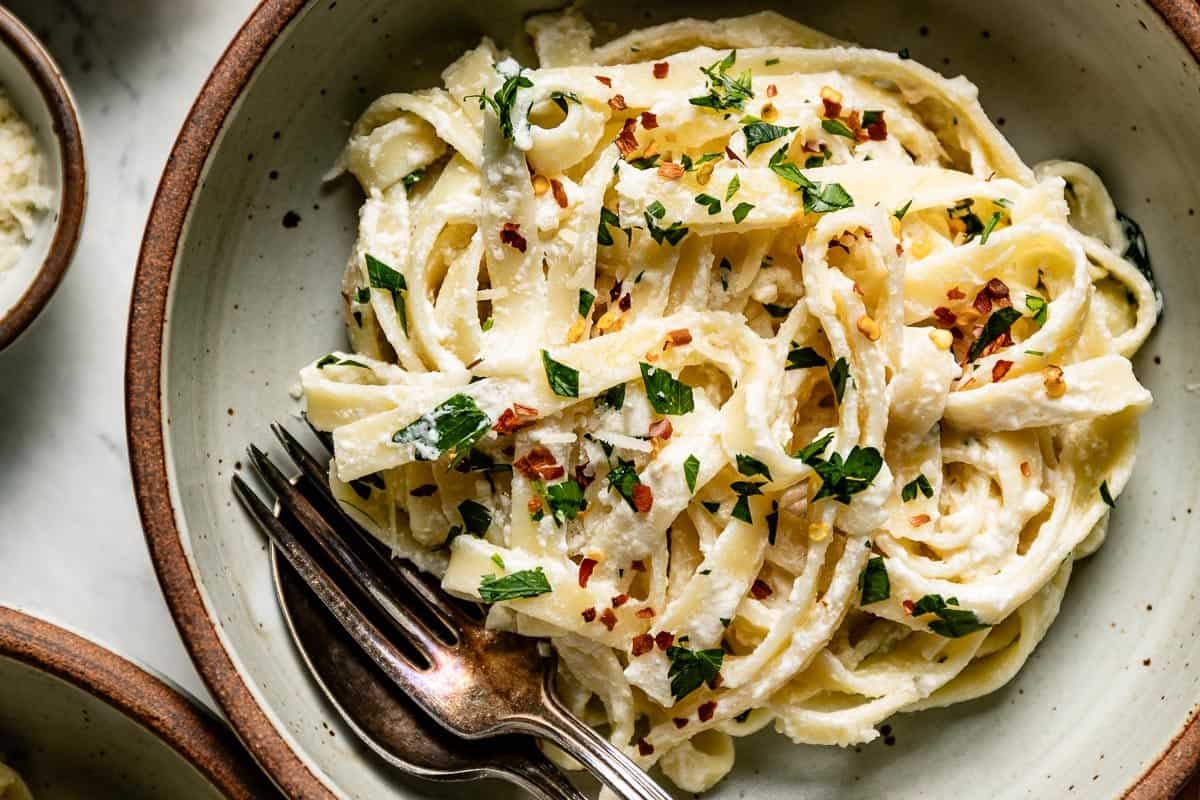 A large bowl of creamy fettuccine made with a Greek yogurt pasta sauce, topped with fresh parsley and red pepper flakes.