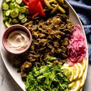 Beef shawarma on a platter with tahini sauce and vegetables.