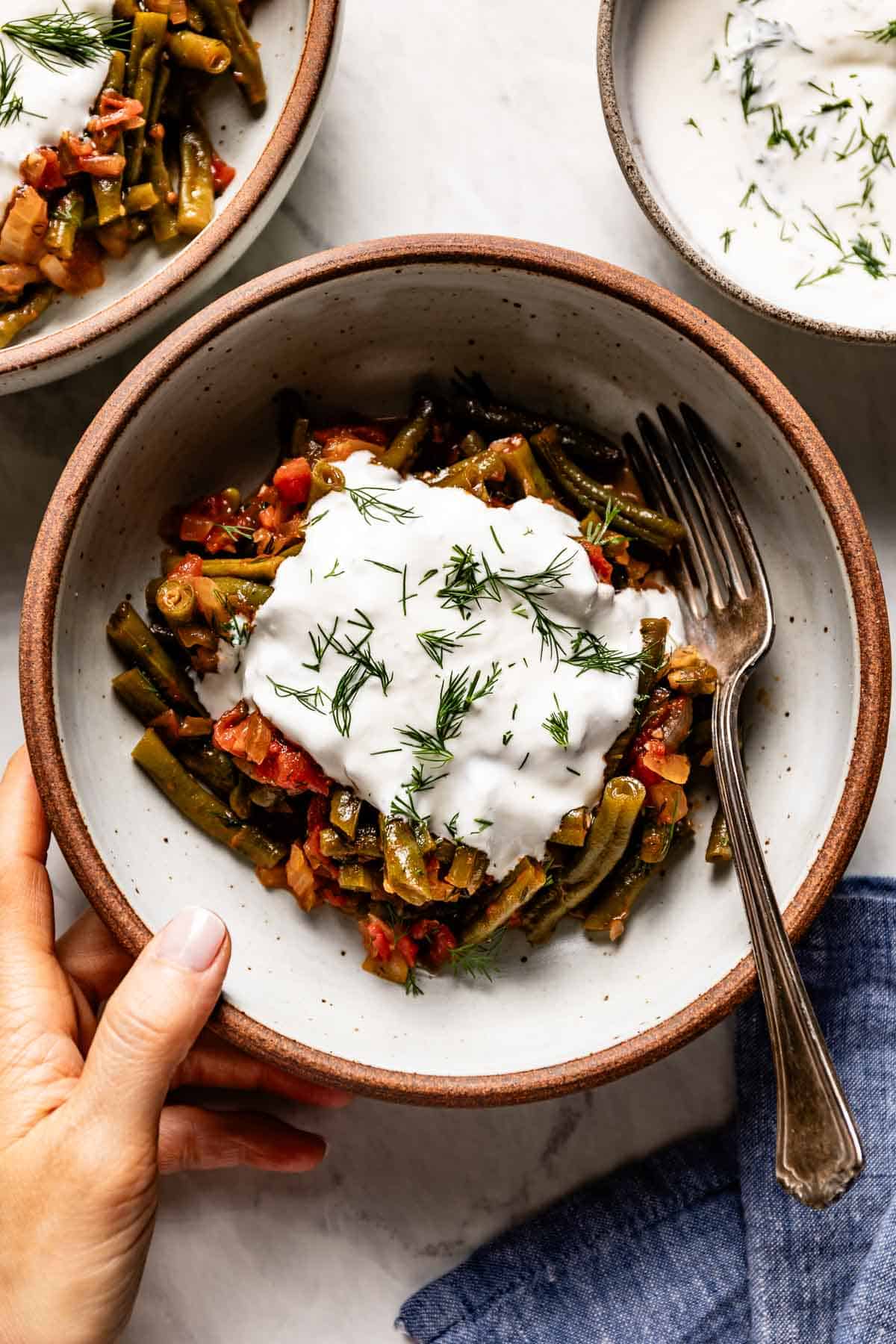 Turkish stewed green beans drizzled with yogurt sauce in a bowl.