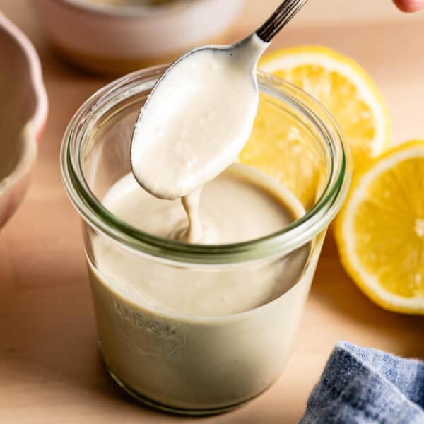 Lemon tahini sauce with a spoon in a jar from the front view.