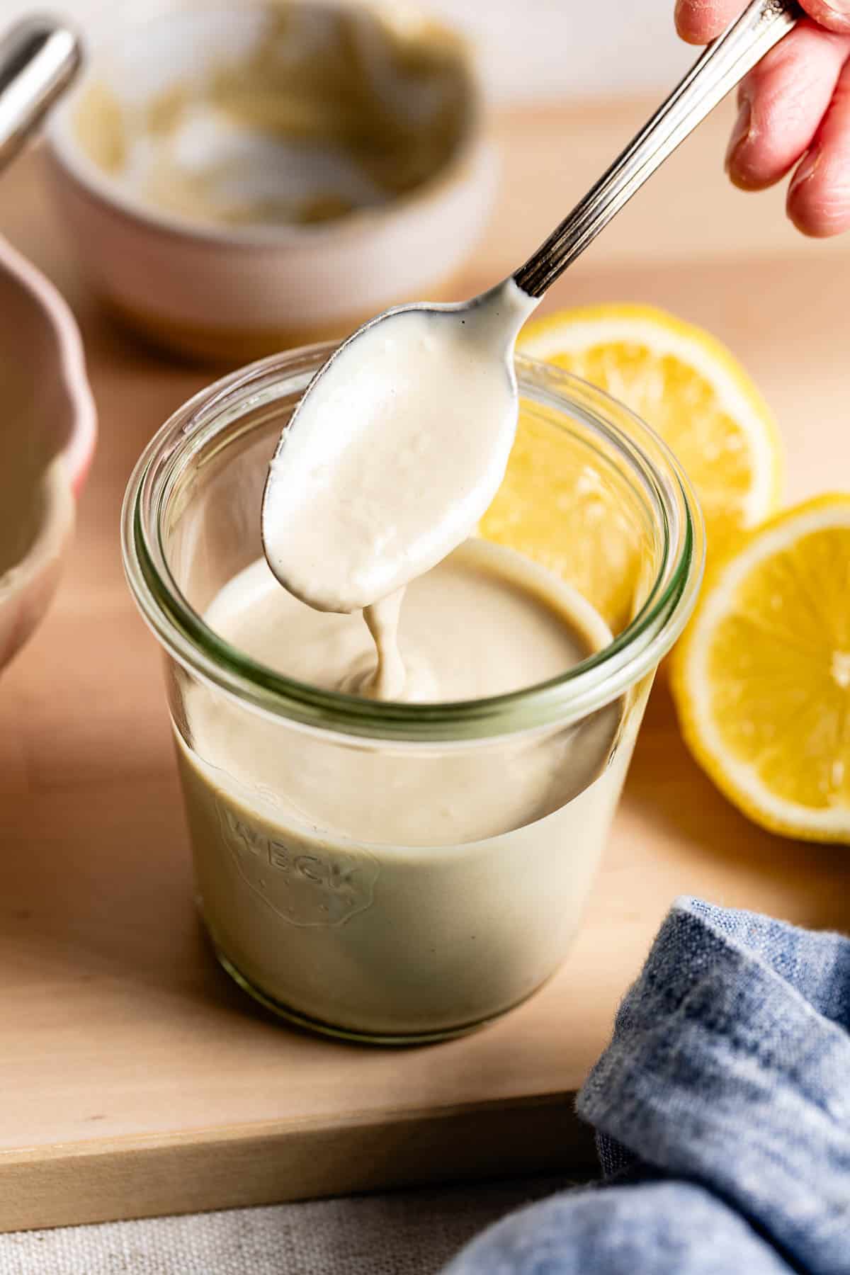 Lemon tahini sauce with a spoon in a jar from the front view.