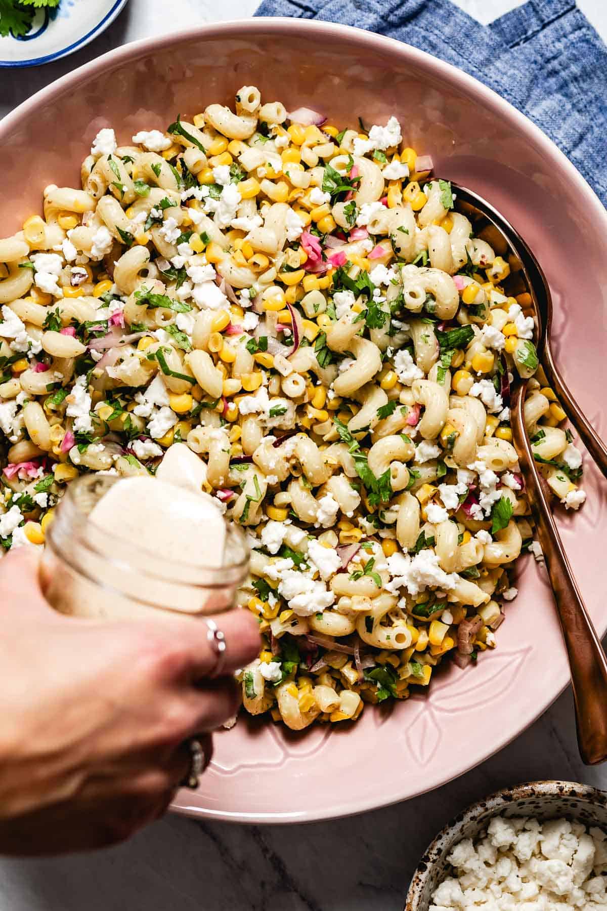 A person is drizzling the elote pasta salad with chili lime dressing.