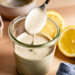 A spoon of lemon tahini sauce drizzling in a jar showing how creamy it is.
