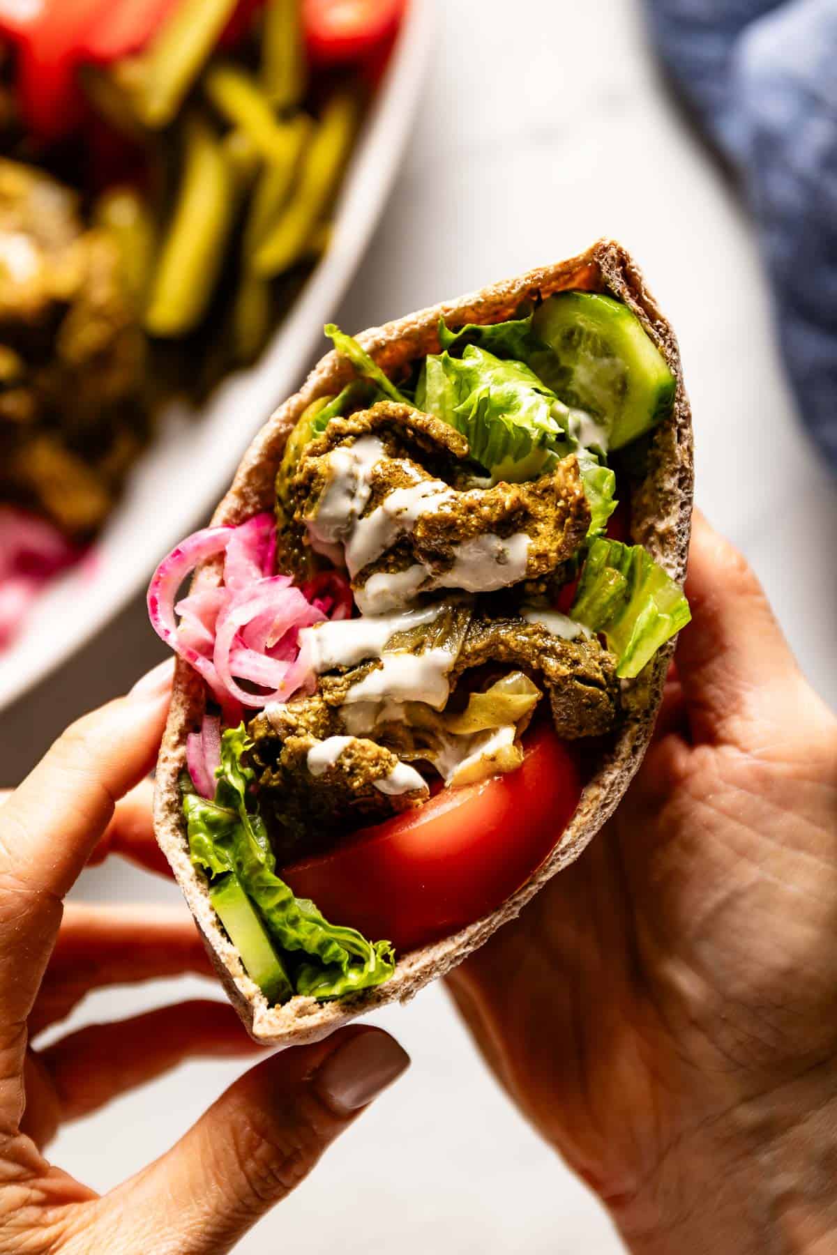 Beef shawarma sandwich drizzled with tahini sauce in someones hands.