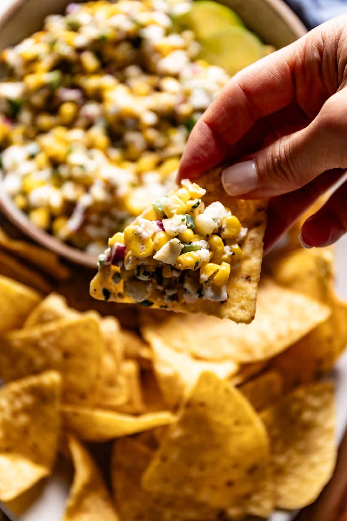 Person serving a chip with Mexican elote dip.