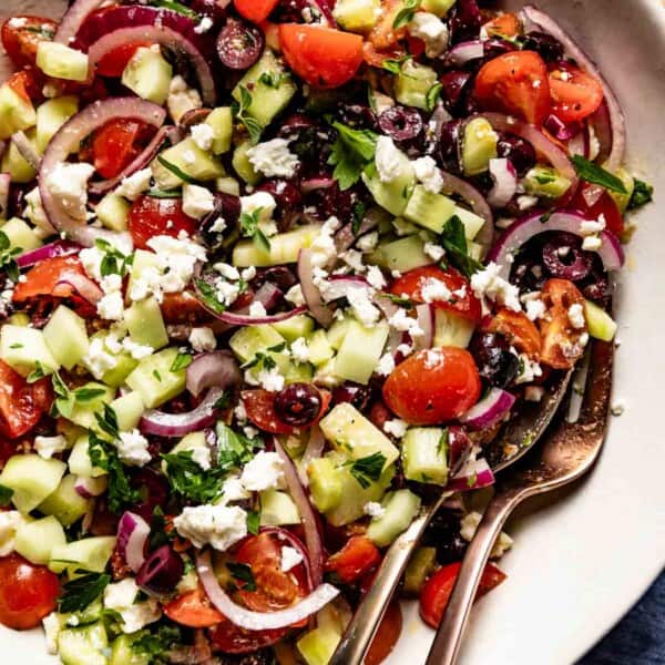 Greek cucumber salad in a bowl with serving ware on the side.