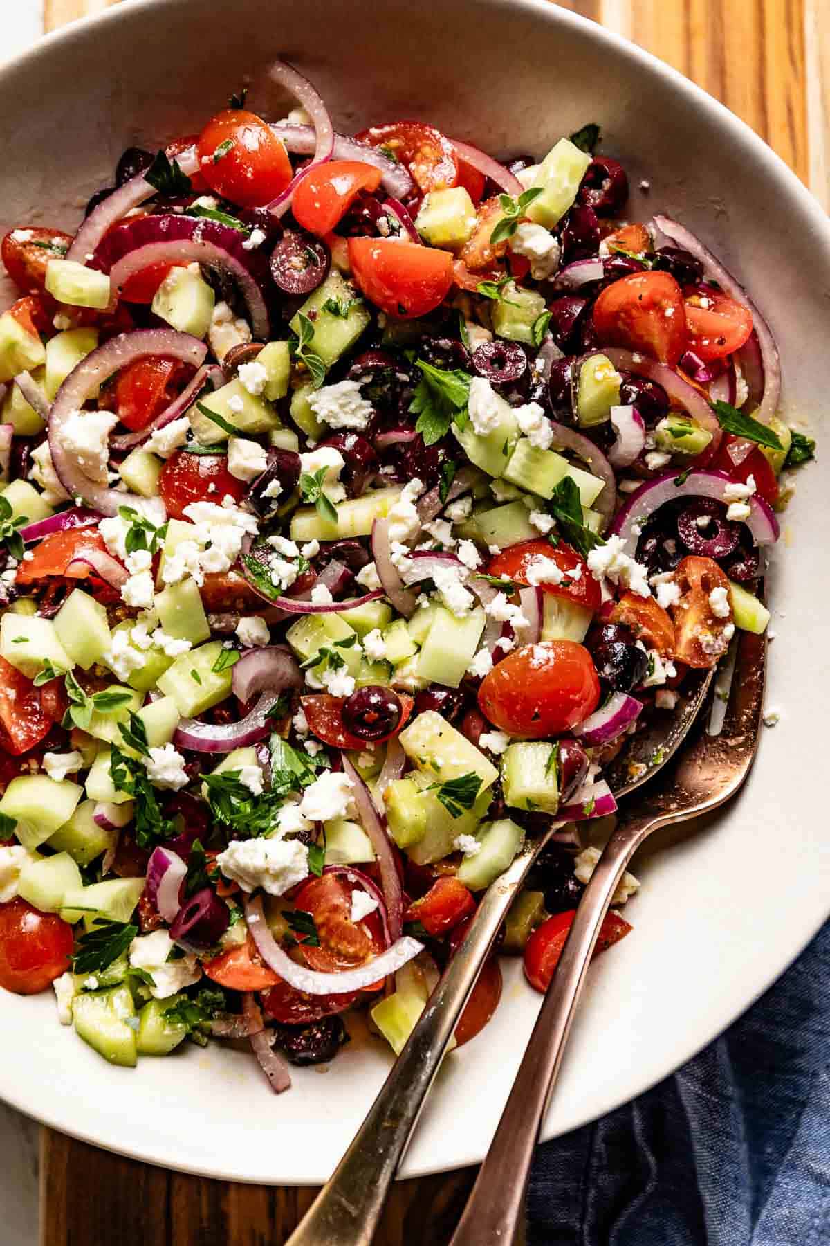 Greek cucumber salad in a bowl with serving ware on the side.