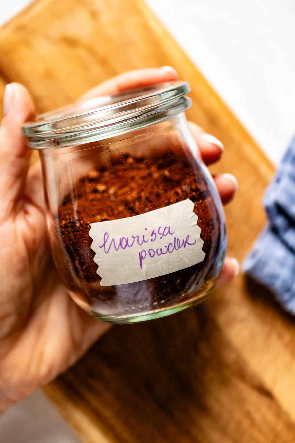 Person holding a jar of homemade harissa spice blend in her hand.