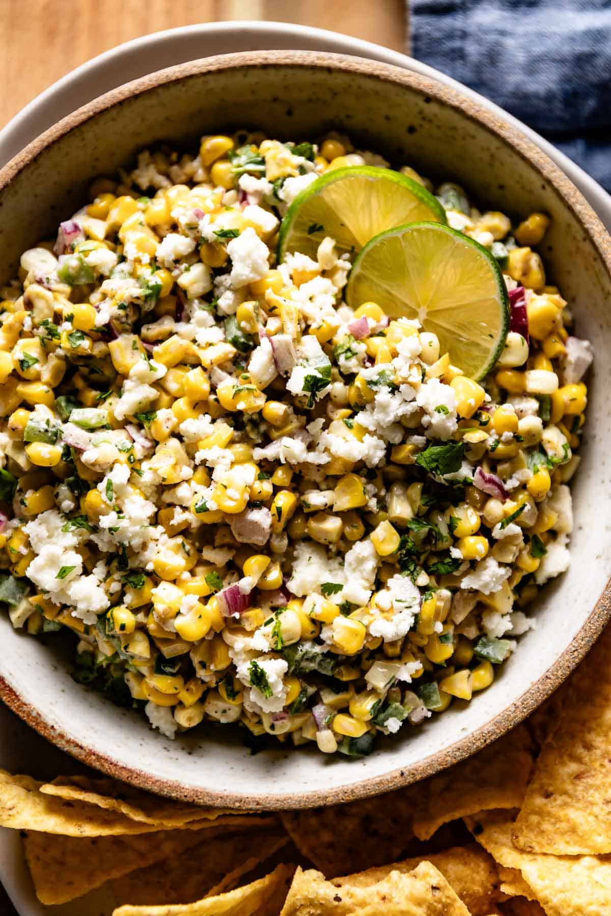 Elote corn dip in a bowl garnished with lime with chips on the side. 