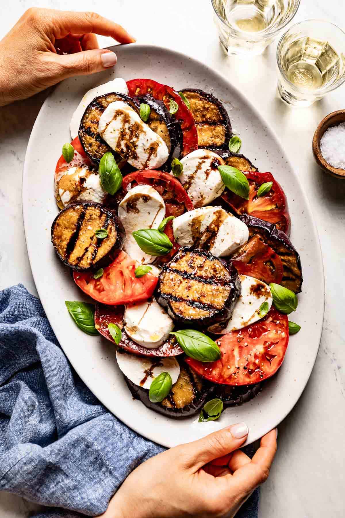 Person serving eggplant Caprese salad along with wine.