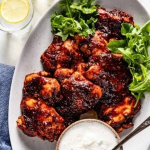 Honey harissa chicken on a plate served with tzatziki on the side.