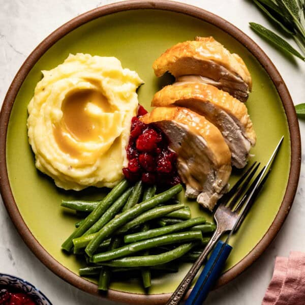 Roasted turkey breast sliced and served with mashed potatoes, gravy, and green beans on a plate.