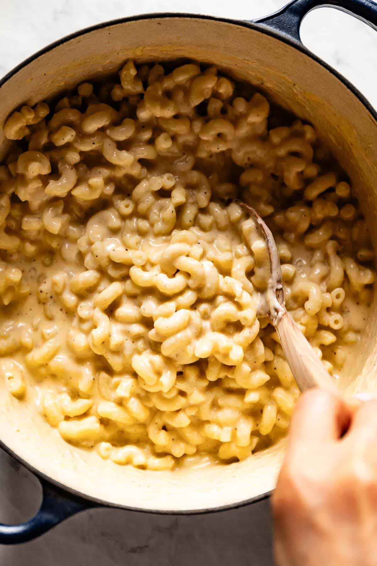 Mac n cheese with cottage cheese in the pot being stirred by a person from the top view.