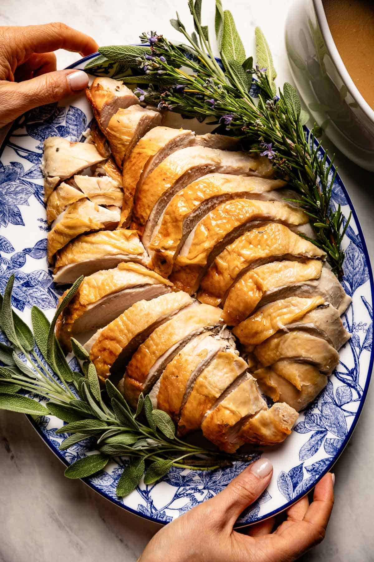 Person serving sliced roasted turkey breast with gravy on the side.