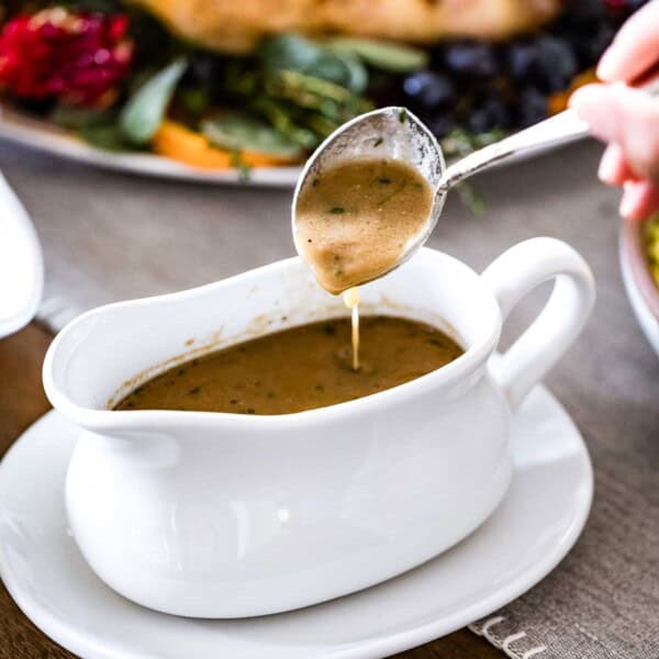 Turkey gravy from drippings in a gravy boat with a spoon drizzling.