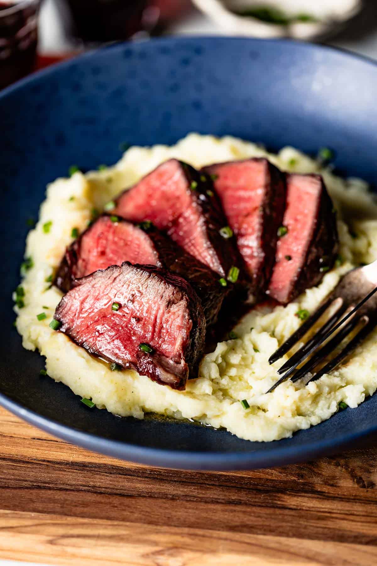 Reverse seared steak sliced and served on a bed of mashed potatoes.