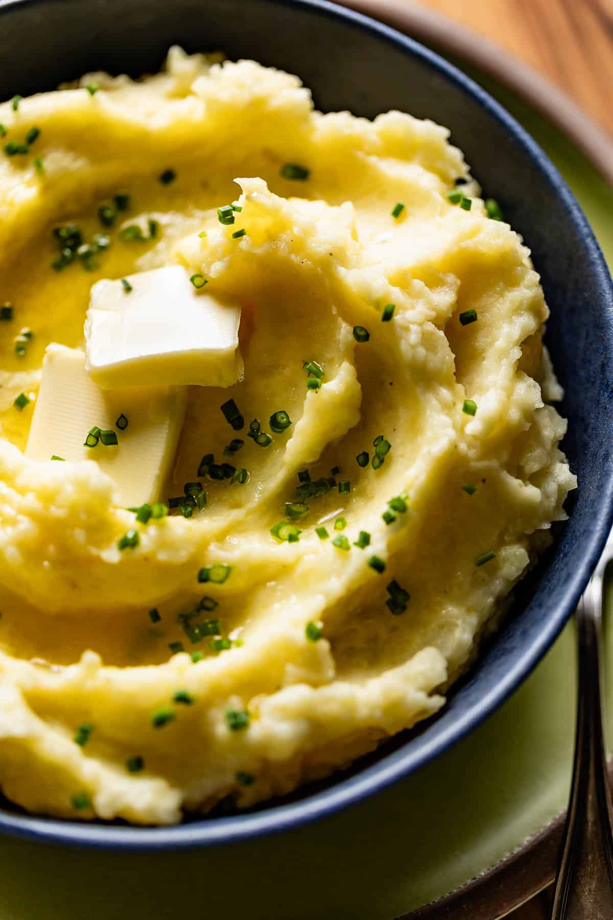 Mashed golden potatoes in a bowl garnished with butter and chives.