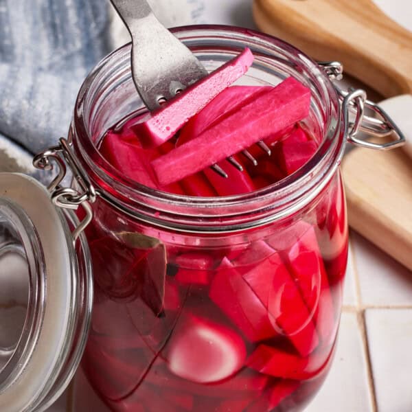 Middle Eastern pickled turnips in a jar with a few of them held in a fork.